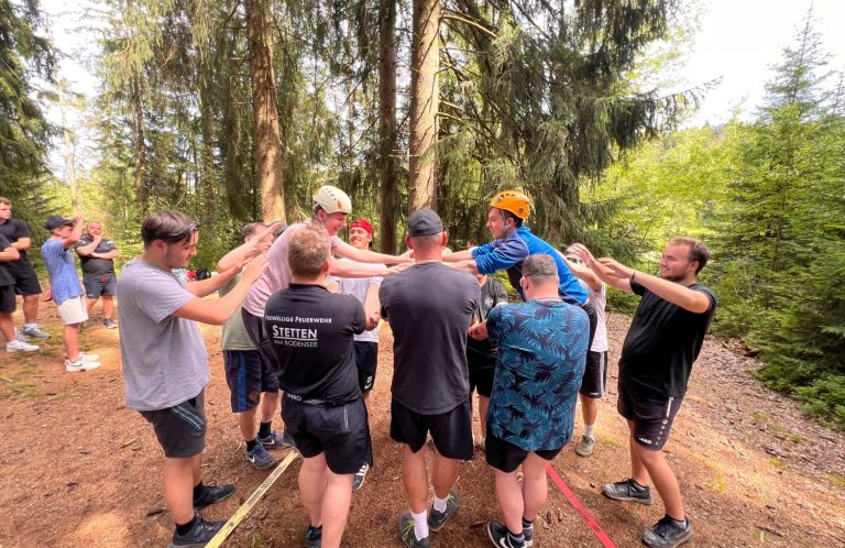 Gemeinsam Balance finden Teilnehmende unterstützen sich gegenseitig bei einer Balanceaufgabe im Wald.
