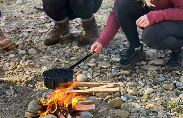 Draußen gemeinsam Neues ausprobieren Zwei Teilnehmende kümmern sich gemeinsam um ein kleines Feuer im Freien.