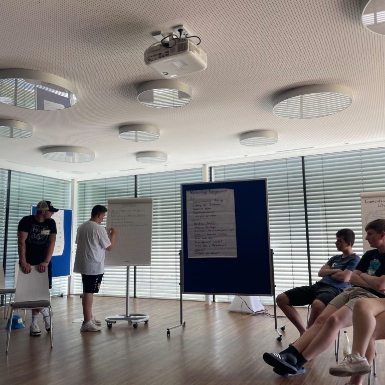 Erwartungen sichtbar machen Teilnehmende erläutern ihre Themen an Moderationswänden vor einer Seminargruppe.