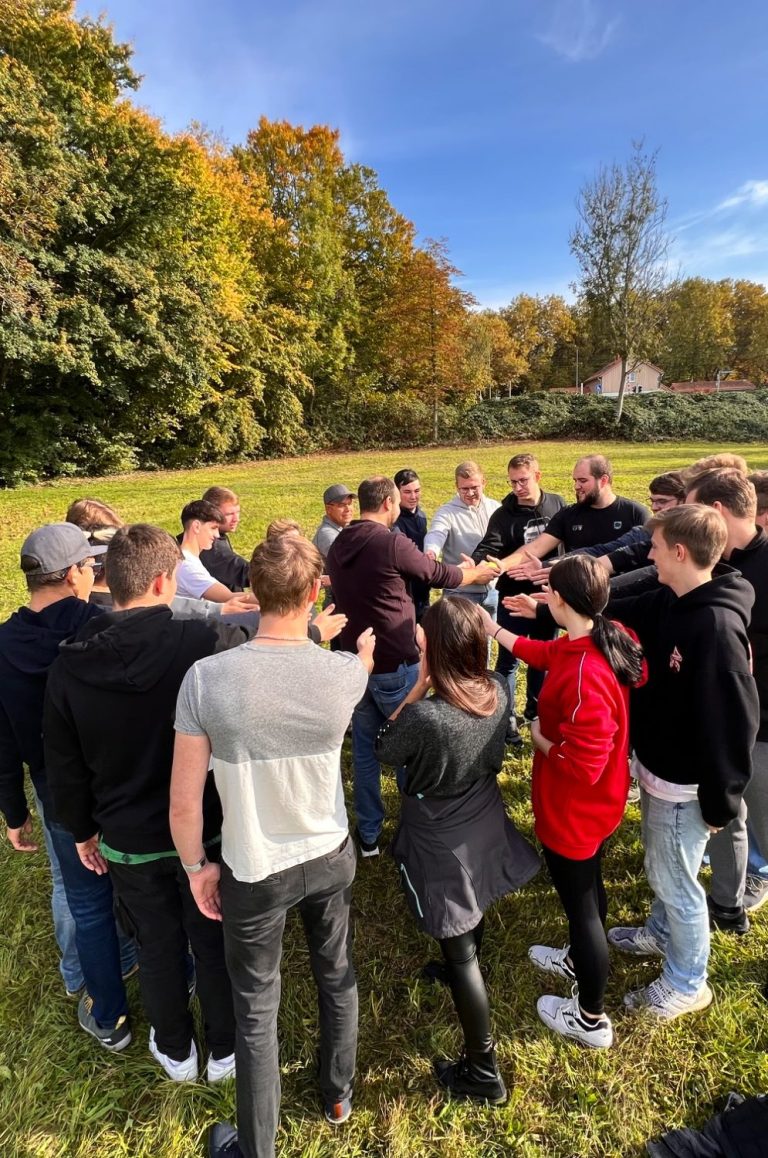 Als Ausbildungsgruppe zusammenfinden Junge Teilnehmende finden bei einer gemeinsamen Aufgabe auf einer Wiese als Gruppe zusammen.