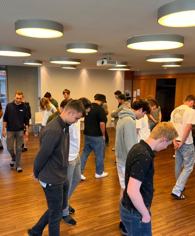 In Bewegung miteinander ankommen Junge Teilnehmende begegnen sich bei einer gemeinsamen Aktivität im Seminarraum.