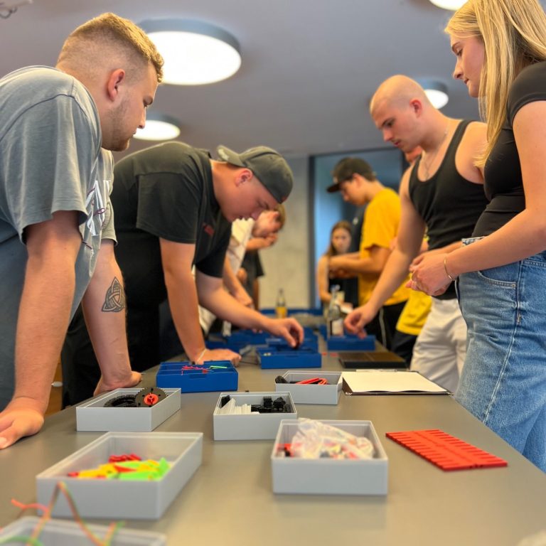 Zusammenarbeit wird im Tun sichtbar Mehrere Teilnehmende arbeiten konzentriert gemeinsam an einer kooperativen Aufgabe am Tisch.