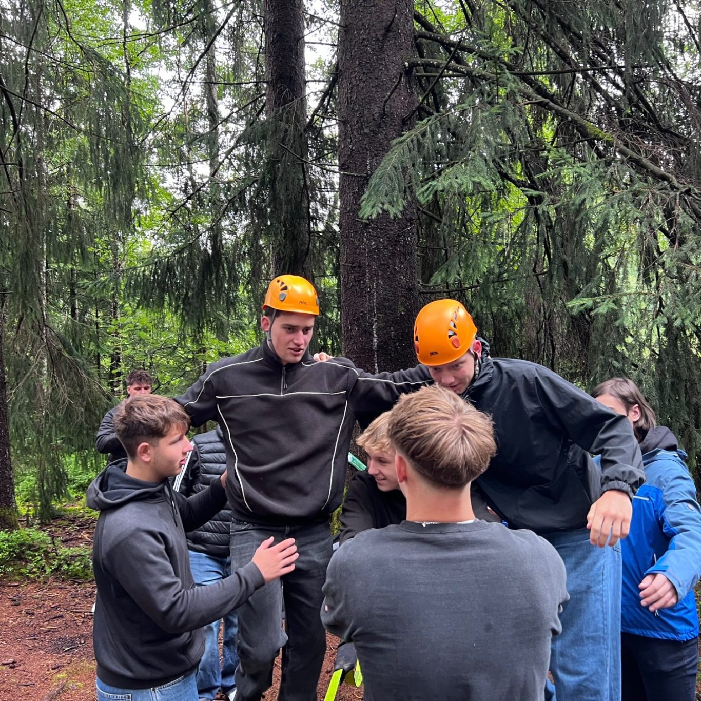 Vertrauen wächst durch gemeinsame Erfahrung Teilnehmende unterstützen und sichern sich bei einer gemeinsamen Aufgabe im Wald.